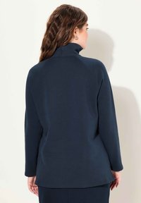 Mörkblå långärmad tröja med hög krage, med en mjuk textur och raglanärmar, utformad för komfort och rörelsefrihet.