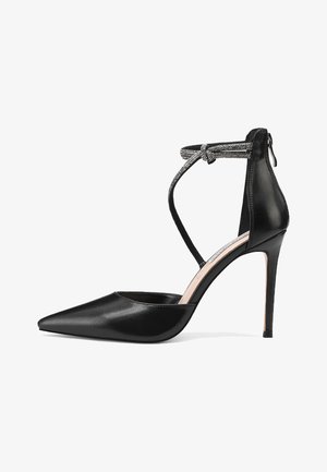 Scarpa con tacco alto in pelle verniciata nera, con punta affusolata, cinturino alla caviglia e dettaglio metallico, caratterizzata da un design elegante e da un sottile tacco a stiletto.