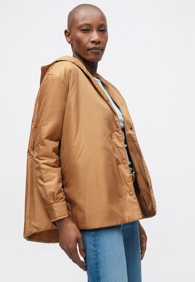 Brun polstret jakke med hætte, trykknapper og en afslappet pasform; båret over en lyseblå top, parret med lyse denim jeans.