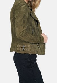 Olive green suede biker jacket with a zip closure, side pocket zippers, and two buckle accents on the back, featuring a fitted design.