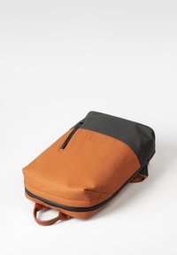 Een oranje en zwarte rugzak met een ritsvak aan de voorkant, gemaakt van soepel leer, met een rechthoekige vorm en een handvat aan de bovenkant.