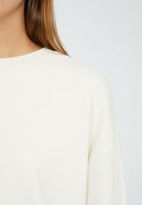 Krémový oversized svetr s kulatým výstřihem. Měkká, hladká tkanina a spadlá ramena vytvářejí uvolněný střih. Bez viditelných vzorů nebo akcentů.