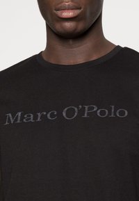Schwarzes Baumwoll-T-Shirt mit Rundhalsausschnitt und dem Logo "Marc O’Polo" in grauer Kontrastschrift auf der Brust.