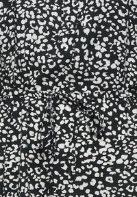 Tissu noir avec un motif léopard blanc irrégulier et un nœud à la taille au centre.
