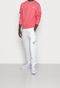 Rosa Nike sweatshirt med en vit logotyp, kombinerat med vita cargobyxor med sidofickor och en multikolor Nike swoosh. Vita sneakers.