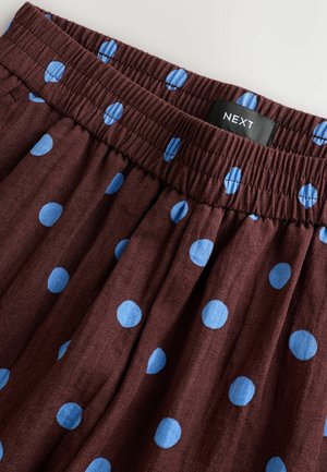 Brown fabric skirt with blue polka dots and elastic waistband, showing a black NEXT brand label sewn inside.