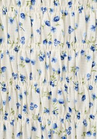 Tissu blanc avec de petites fleurs bleues et des tiges vertes, présentant une texture froncée élastique en rangées horizontales.