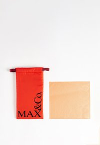Buzunar din țesătură roșie cu șnur, având inscripționat cu text negru "MAX & Co." lângă un pătrat bej cu un logo subtil embosat. Textură netedă.