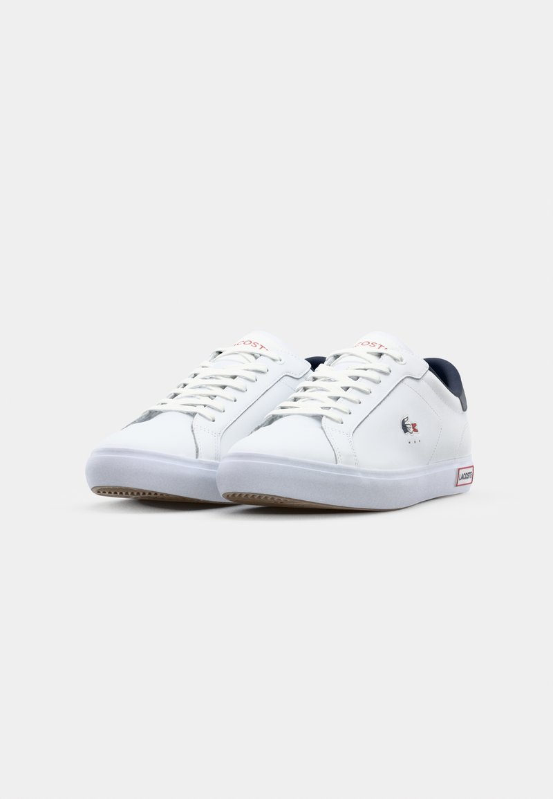 Białe sneakersy z gładkiej syntetycznej skóry, granatowe akcenty, sznurowane zapięcie i gumowa podeszwa; na boku i języku znajduje się logo Lacoste.