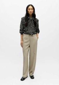 Czarna i biała wzorzysta bluzka z długim rękawem i kokardą, w zestawieniu z beżowymi spodniami o szerokich nogawkach i czarnymi loafersami.