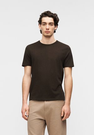 Brown short-sleeve t-shirt in cotton fabric, featuring a round neck and a fitted shape, paired with light-colored textured trousers.