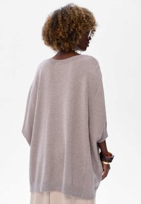 Jasnoszary, oversize sweter z szerokim dekoltem, opadającymi ramionami i prążkowanym dołem. Miękka struktura z minimalnymi detalami i bez wyraźnych wzorów.