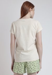 Camiseta de manga corta color crema con cuello redondo, combinada con pantalones cortos verde claro que presentan un patrón de dibujos animados repetido.