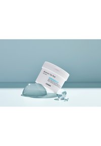 Witte ronde container met het label "Moisture UP Pad" van COSRX, schuin gehouden met lichtblauwe accenten. Duidelijke gelachtige druppels zijn dichtbij geplaatst op een lichtblauwe ondergrond.