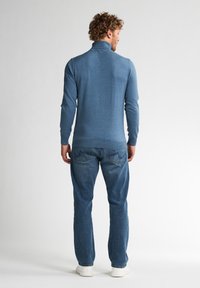 Suéter azul de manga larga y cuello alto con un diseño ajustado, puños y dobladillo acanalados. Combinado con jeans de mezclilla azul claros y zapatillas blancas.