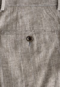 Barna és krémszínű kutyacukor mintájú szövet, melyen egyetlen sötét gomb és függőleges csíkok találhatók, texturált szövésű és szabott zsebrészlettel.