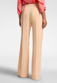 Pantaloni beige a gamba larga realizzati in un tessuto liscio con una vita sartoriale. I pantaloni presentano una finitura pulita all'orlo e nessuna tasca visibile.