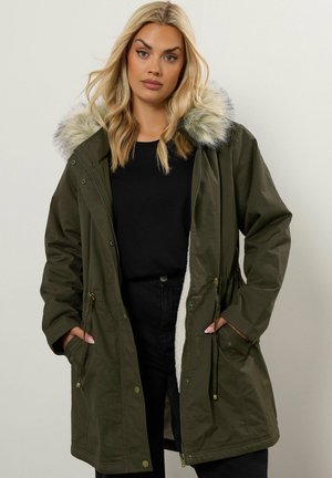 Olivgrüner Parka mit Kunstpelzbesatz an der Kapuze, Reißverschluss und Druckknopfverschlüssen, Kordelzug in der Taille und seitlichen Taschen, die mit weichem Material ausgekleidet sind.