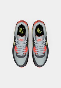 Le sneakers Nike Air presentano una tomaia grigia con dettagli neri, evidenti arancioni brillanti e una finitura testurizzata. Includono lacci grigi e logo.