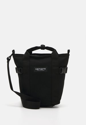 Bolso negro de material de lona resistente, con asas cortas, correa de hombro ajustable y un parche de logo en la parte frontal. Presenta cierres de hebilla.