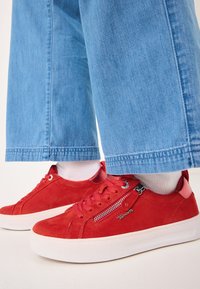 Sneakers in suede rosso con suole in gomma bianca, dotati di una cerniera laterale decorativa, design con punta tonda e lacci rossi abbinati.