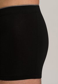 Černé boxerky vyrobené z měkké tkaniny. Obsahují hladký pas s kontrastním stehem, těsný střih a jednoduchý, čistý design.