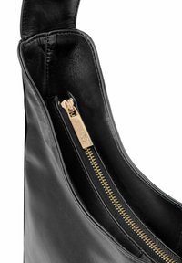 Wnętrze czarnej skórzanej torebki na ramię z złotym zamkiem błyskawicznym, gładką fakturą i czystymi liniami. Odszycie zamka zawiera detal z brandingiem.