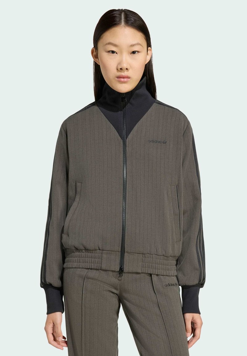 Sivá rebrovaná bunda na zips s vysokým golierom, čiernymi akcentmi, bočnými vreckami a priliehavým pásom. V páre s rovnakými nohavicami.