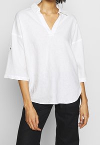 Maglione bianco in lino con scollo a V e maniche a tre quarti, caratterizzato da una vestibilità rilassata e dettagli di cucitura sottili.