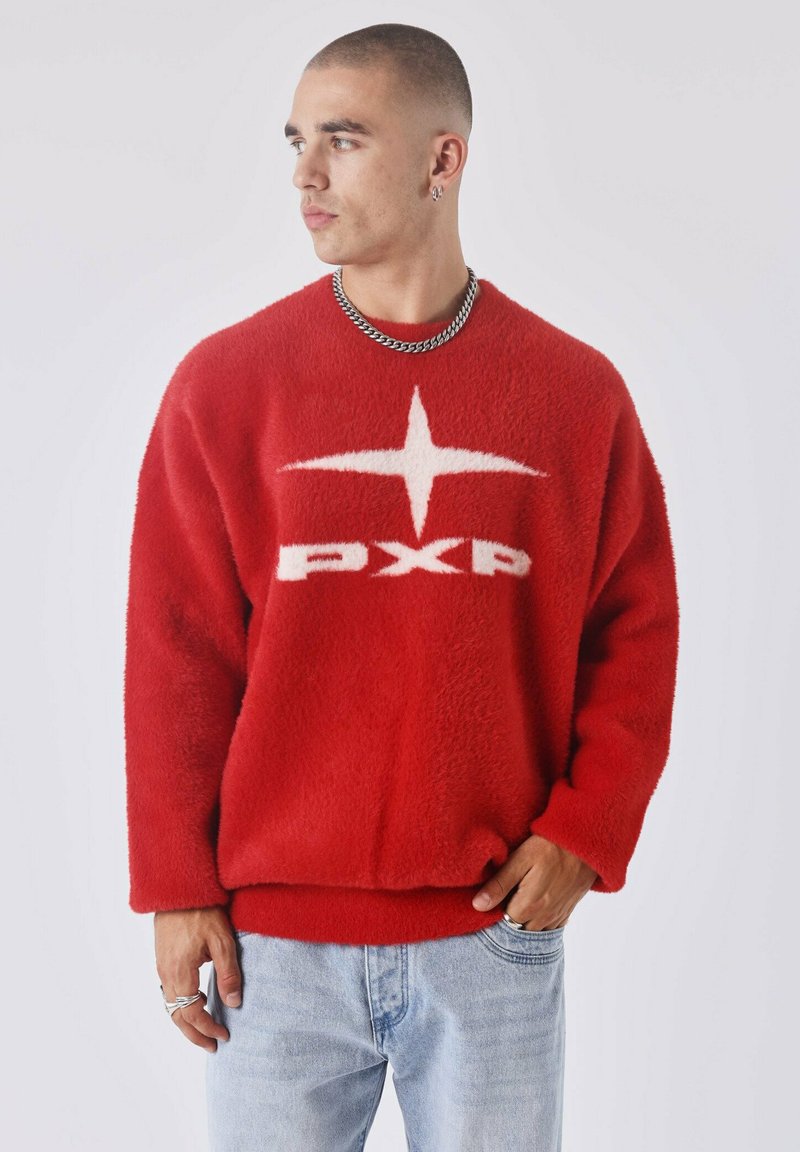Rode fleece trui met een losse pasvorm, voorzien van een wit sterrenlogo en de letters "PXP" over de borst, gecombineerd met lichtblauwe spijkerbroek.