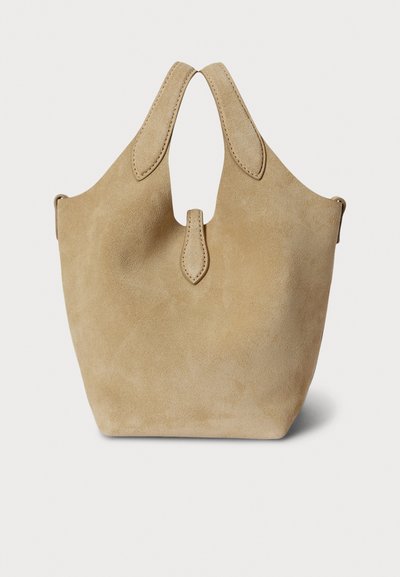 Τσάντα ώμου από μπεζ σουέντ με κωνικό σχέδιο, κοντά χερούλια και κεντρικό άνοιγμα για εύκολη μεταφορά. Απαλή υφή με ελάχιστες λεπτομέρειες.