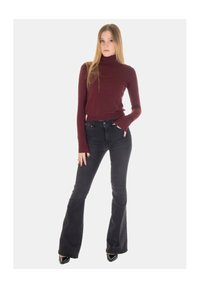 Maglione a collo alto color bordeaux abbinato a jeans svasati neri; l'outfit presenta un design aderente e maniche lunghe, con una texture liscia.