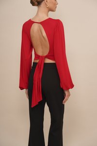 Red long-sleeved top with an open back, tied at the waist. Paired with black pants, showcasing a smooth fabric and relaxed fit.