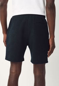 Black shorts with a textured herringbone pattern, featuring a back pocket and an elastic waistband for comfort.