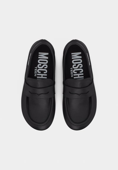 Paire de mocassins noirs à enfiler avec bouts arrondis et détail de sangle, affichant la marque "Moschino Teen" à l'intérieur.
