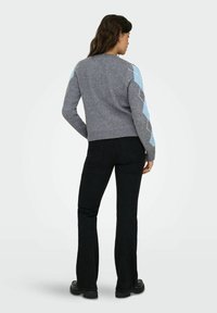 Grijze trui met een blauw ruitenpatroon op de mouwen, geribbelde boorden en zoom. Gecombineerd met aansluitende zwarte broek en zwarte schoenen.
