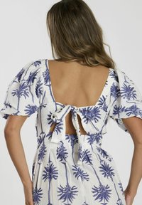 Vestido blanco con estampado de palmeras moradas, diseño de mangas abullonadas, espalda abierta con detalle de lazo. Tela ligera, hasta la rodilla.