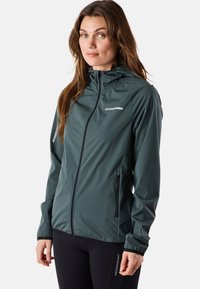 Veste technique de plein air, verte foncée, avec fermeture éclair à l'avant, capuche ajustable, deux poches latérales, tissu léger, texture lisse, logo minimaliste.