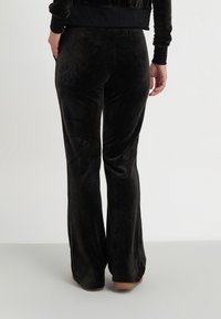Pantalones acampanados negros y aterciopelados con una textura suave, que cuentan con una cintura alta y ajustados a través de las caderas, ensanchándose hacia la pierna.