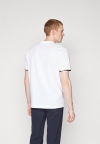 Weißes Polohemd mit klassischem Design, ausgestattet mit kurzen Ärmeln und schwarzen Streifenakzenten an den Bündchen. Einfache, glatte Baumwollstruktur.