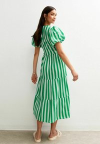 Robe maxi à rayures vertes avec des manches bouffantes, design à volants et taille cintrée. Tissu doux avec des rayures verticales blanches. Chaussures en sable.