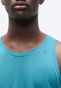 Débardeur de sport turquoise clair avec un col rond, un tissu texturé et un petit logo rond en accent sur l'épaule.