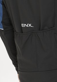 Schwarze Sportjacke mit elastischem Bund, auffälligem weißen "ENX"-Logo und blauen Akzenten im oberen Bereich. Weiche, glatte Stofftextur.