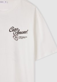 Biała bawełniana koszulka z krótkim rękawem, z czarnym nadrukiem tekstu, w tym "Ciao Amore!" oraz grafiką serca, o luźnym kroju.