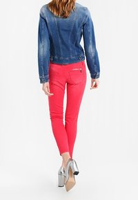 Džínová bunda s přiléhavým střihem, modré barvy a vybledlými detaily, doplněná o přiléhavé růžové kalhoty a stříbrné vysoké podpatky.