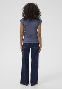 Marinblå kortärmad topp med en figurnära siluett, matchad med vida blå denimjeans med bakfickor och synliga sömdetaljer.