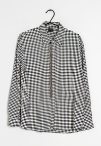 Svart- och vitrutigt långärmat skjorta med krage och knappstängning fram. Har en kedjeaccent längs knappslån.