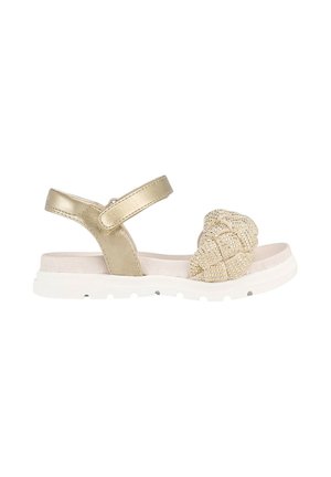 Sandalia beige con suela blanca acolchada, tira metálica alrededor del tobillo y tira frontal trenzada con cuentas.
