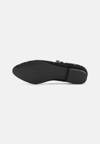 Chaussure en suède noir avec un bout arrondi, une semelle plate et des clous décoratifs. Semelle intérieure texturée et semelle extérieure en caoutchouc lisse pour une adhérence améliorée.