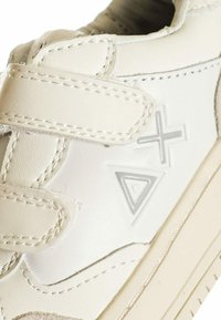 Sneaker in pelle bianca con cinturino in velcro, con accenti geometrici grigi e dettagli di cucitura su una suola testurizzata.